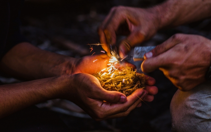 a person holds kindling in their hand while another works to light a spark 